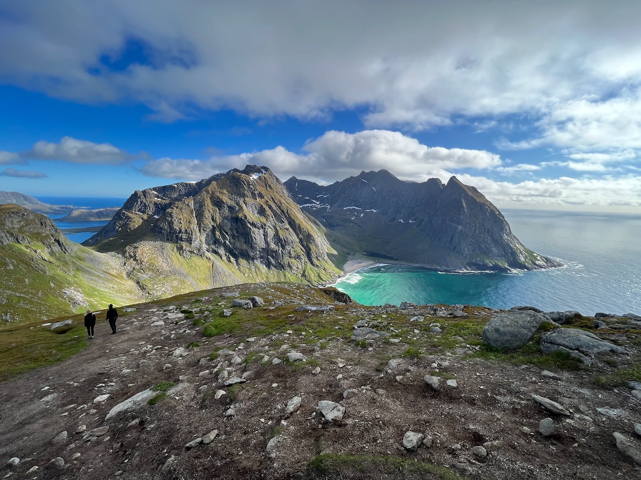 Walkers on a rocky Norwegian headland above a white-sand bay